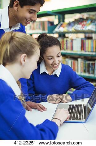 Stock Image - Students working with laptop in library and smiling. Fotosearch