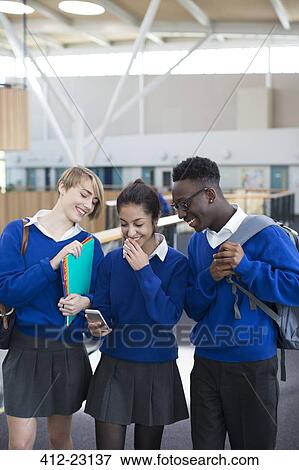 Three happy students wearing school uniforms using smartphone in school corridor View Large Photo Image Stock Photo - Three happy students wearing school uniforms using smartphone in school corridor. Fotosearch