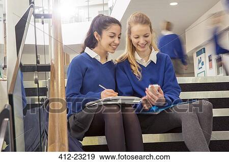 Two female students wearing blue school uniforms sitting on steps in school corridor and looking at mobile phone View Large Photo Image Stock Photo - Two female students wearing blue school uniforms sitting on steps in school corridor and looking at mobile phone. Fotosearch