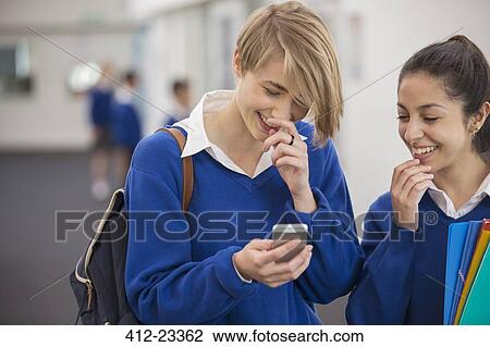Stock Image - Two smiling female students looking at mobile phone in school corridor. Fotosearch