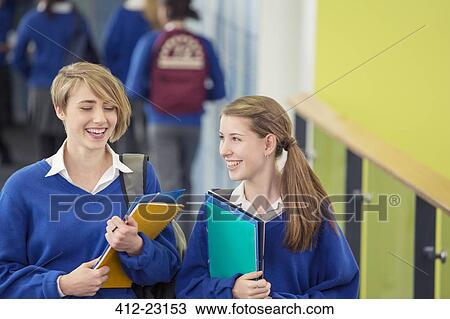 Stock Image - Two smiling female students wearing school uniforms walking through school corridor. Fotosearch