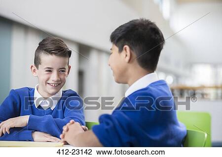 Two smiling schoolboys wearing school uniforms talking at desk in classroom View Large Photo Image Stock Image - Two smiling schoolboys wearing school uniforms talking at desk in classroom. Fotosearch