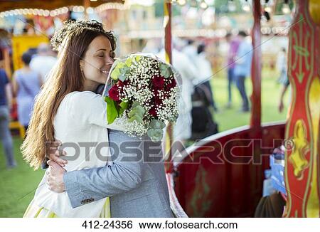 Stock Photograph - Woman holding bouquet and embracing his boyfriend in amusement park. Fotosearch