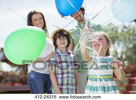 Young girl holding bunch of balloons, family standing behind her View Large Photo Image Stock Photography - Young girl holding bunch of balloons, family standing behind her. Fotosearch