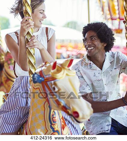 Young multiracial couple smiling on carousel in amusement park View Large Photo Image Stock Photograph - Young multiracial couple smiling on carousel in amusement park. Fotosearch