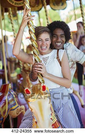 Stock Photography - Young multiracial couple smiling on carousel in amusement park. Fotosearch