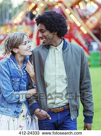 Stock Image - Young multiracial couple smiling to each other in amusement park. Fotosearch