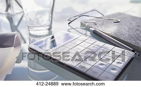 Stock Photo - "Close up of desk with calculator, glass, pen and notepad". Fotosearch