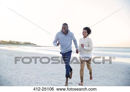 Stock Photograph - Couple holding hands and running on beach. Fotosearch