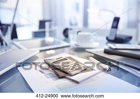 Stock Image - "Desk in modern office filled with supplies, laptop and phone, tablet". Fotosearch