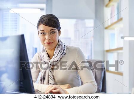 "Female office worker sitting at desk using computer, portrait" View Large Photo Image Picture - "Female office worker sitting at desk using computer, portrait". Fotosearch