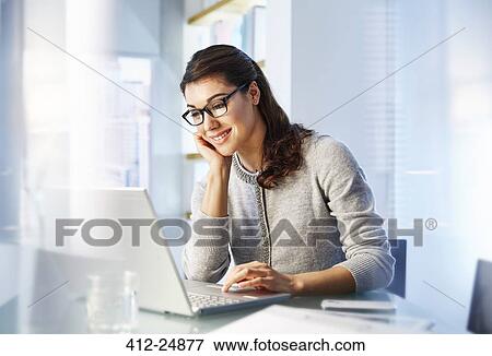 Female office worker sitting at desk using laptop View Large Photo Image Stock Photo - Female office worker sitting at desk using laptop. Fotosearch
