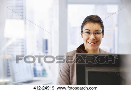 Stock Photo - "Female office worker sitting at desk using computer, portrait". Fotosearch