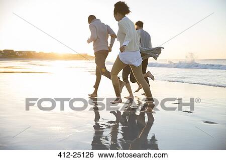 Stock Photograph - Four friends running ob beach in evening sun. Fotosearch