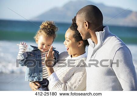 Stock Image - Happy family giving high five on beach. Fotosearch