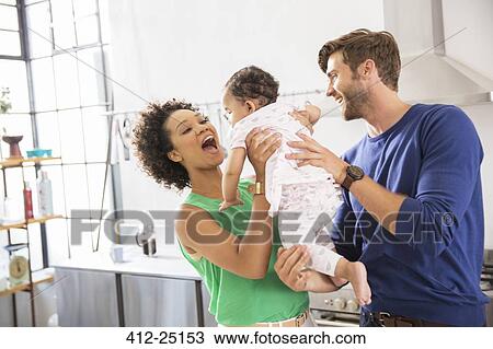 Happy parents holding their baby daughter in domestic kitchen View Large Photo Image Stock Image - Happy parents holding their baby daughter in domestic kitchen. Fotosearch