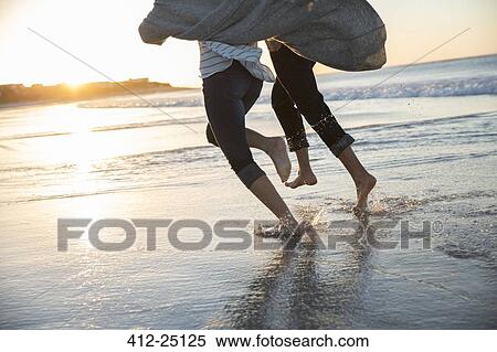 Stock Photography - Legs of young couple running on beach at sunset. Fotosearch