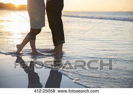 Stock Photo - Legs of young couple standing on beach. Fotosearch