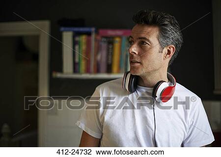 Stock Image - Man at home with red headphones over his neck looking away. Fotosearch