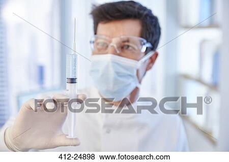 Man in surgical mask and labcoat holding syringe with fluid View Large Photo Image Stock Photo - Man in surgical mask and labcoat holding syringe with fluid. Fotosearch