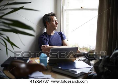 Man sitting at table with open laptop looking through window View Large Photo Image Stock Photo - Man sitting at table with open laptop looking through window. Fotosearch