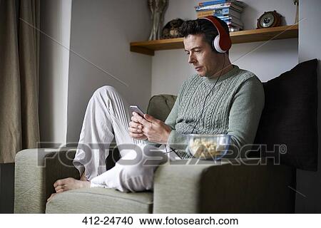 Man sitting in armchair with headphones using smartphone View Large Photo Image Stock Image - Man sitting in armchair with headphones using smartphone. Fotosearch