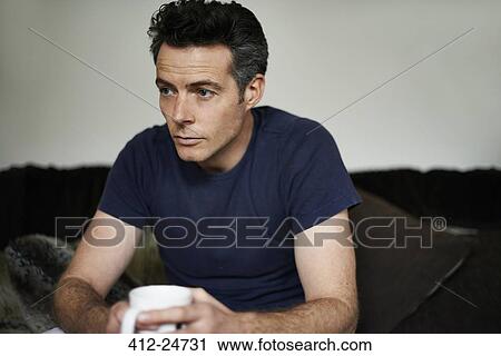 Man sitting on sofa holding mug looking sad View Large Photo Image Stock Image - Man sitting on sofa holding mug looking sad. Fotosearch