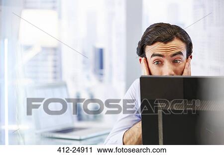 Stock Image - "Man using computer in office, stressed and worried". Fotosearch