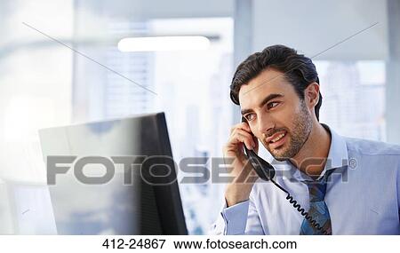Stock Photo - Man using landline phone in office. Fotosearch