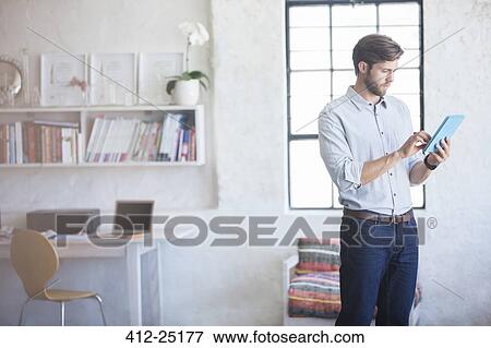 Man with digital tablet standing in home office View Large Photo Image Stock Photo - Man with digital tablet standing in home office. Fotosearch
