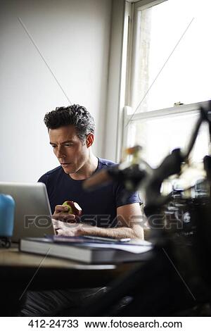 Man working on laptop at home eating apple View Large Photo Image Stock Image - Man working on laptop at home eating apple. Fotosearch