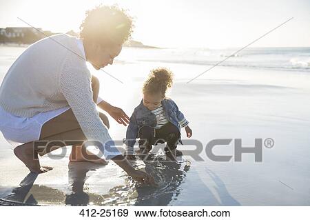 Stock Photo - Mother and daughter drawing on wet sand on beach. Fotosearch