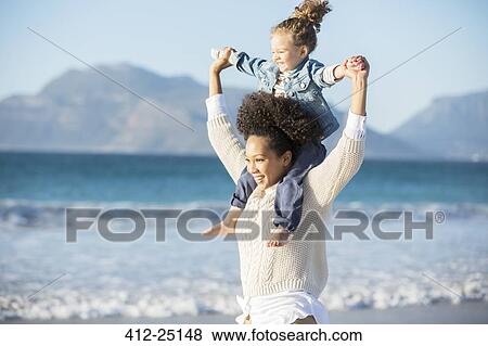 Stock Photo - Mother carrying daughter on her shoulders on beach. Fotosearch