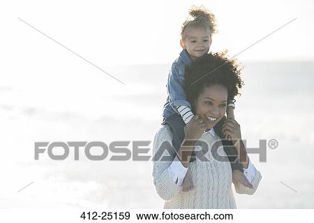 Mother carrying daughter on her shoulders on beach View Large Photo Image Stock Photo - Mother carrying daughter on her shoulders on beach. Fotosearch