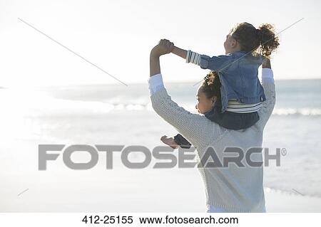 Stock Photography - Mother carrying daughter on her shoulders on beach. Fotosearch