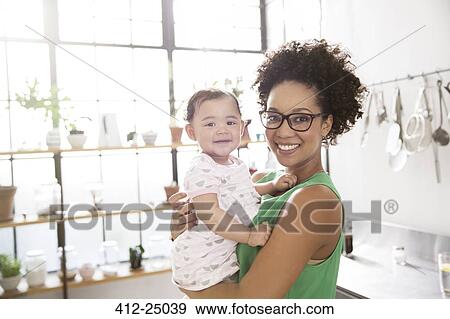Mother holding her baby daughter in domestic kitchen View Large Photo Image Stock Photo - Mother holding her baby daughter in domestic kitchen. Fotosearch