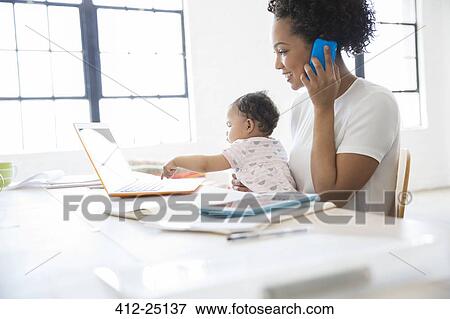 Mother working from home with daughter sitting on her lap View Large Photo Image Stock Photo - Mother working from home with daughter sitting on her lap. Fotosearch