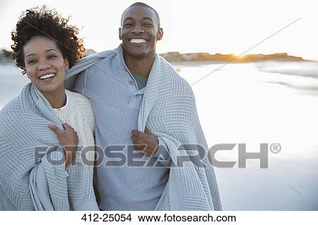 Picture - Portrait of couple wrapped in blanket on beach. Fotosearch