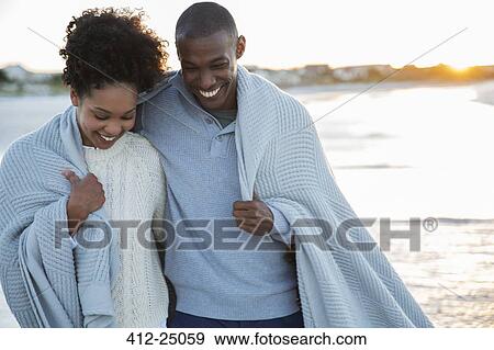 Stock Photo - Portrait of couple wrapped in blanket on beach. Fotosearch
