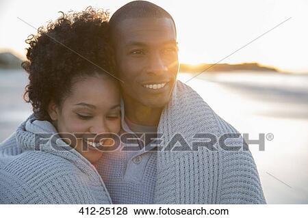 Stock Photo - Portrait of couple wrapped in blanket on beach. Fotosearch