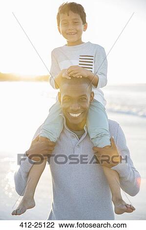 Stock Image - Portrait of father carrying son on shoulders and smiling. Fotosearch
