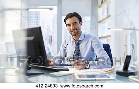 Stock Image - Portrait of man sitting at his desk in office. Fotosearch