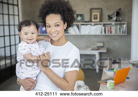 Stock Image - Portrait of mother and baby daughter in home office. Fotosearch