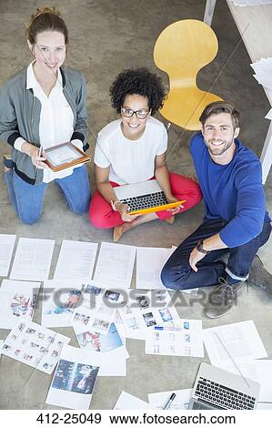 Stock Photo - Portrait of three young people sitting on floor and working together. Fotosearch