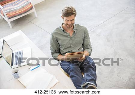Stock Photography - Portrait of young man sitting with legs on desk in studio. Fotosearch