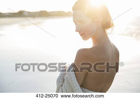Stock Image - Portrait of young woman wrapped in blanket on beach. Fotosearch