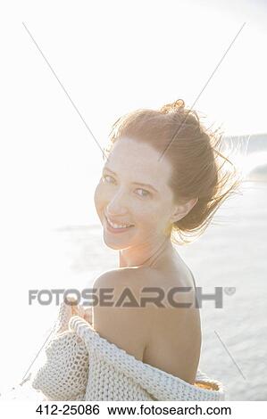 Stock Photograph - Portrait of young woman wrapped in blanket on beach. Fotosearch