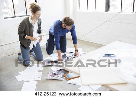 Stock Image - Two young people kneeling on floor and looking at documents. Fotosearch