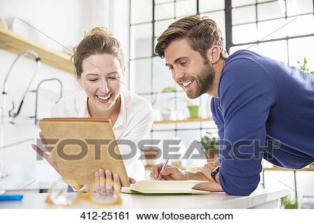 Two young people looking at documents in domestic kitchen View Large Photo Image Stock Image - Two young people looking at documents in domestic kitchen. Fotosearch