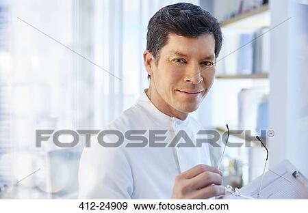 Stock Photo - View of man in laboratory holding glasses looking at camera. Fotosearch